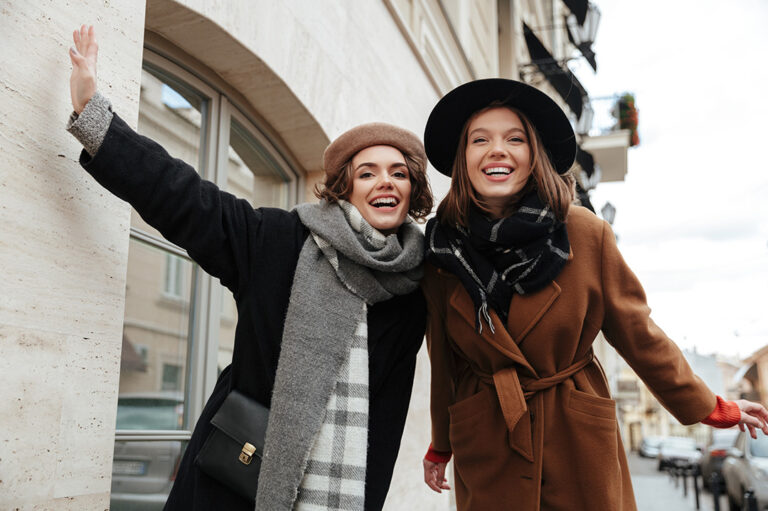 due ragazze vestite con cappotti e cappelli sorridenti per strada